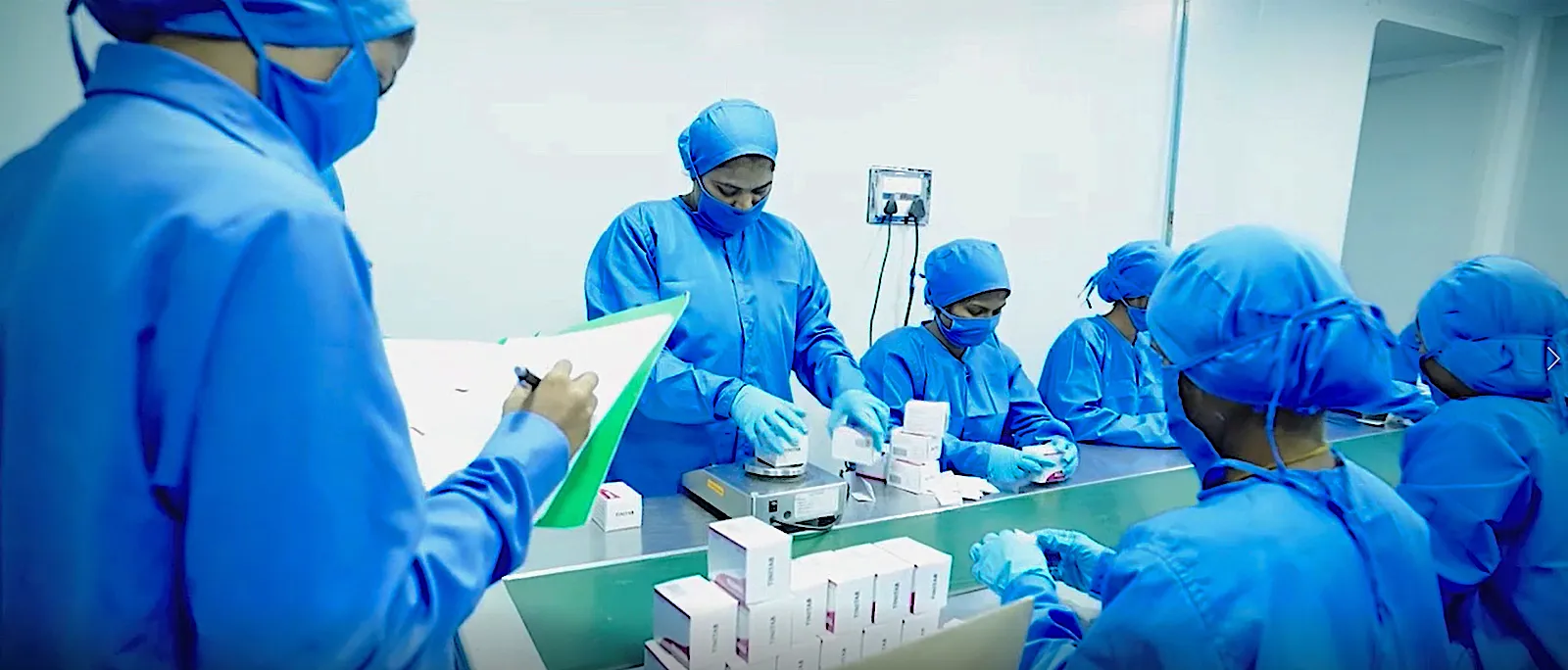 Pharmaceutical clean room with workers in blue protective gear operating modern manufacturing equipment